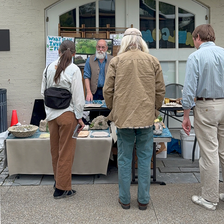 A small crowd of people talk to a vendor at their table.